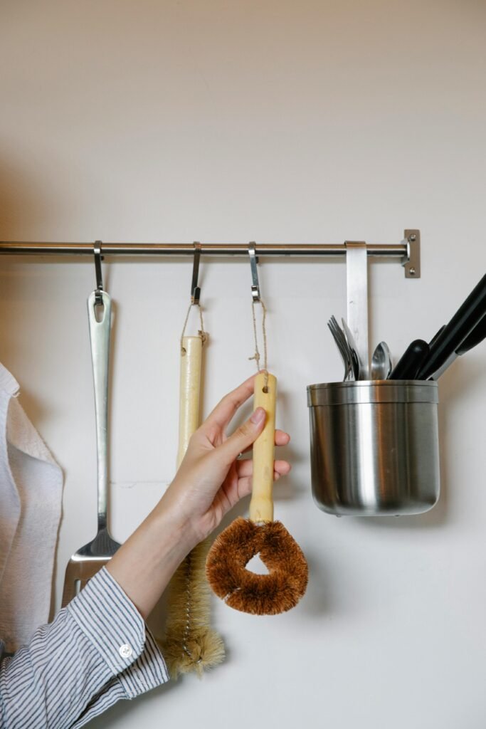 pexels photo 7262362 7262362 Unrecognizable female hanging brush for washing dishes on metal rack on wall with various equipment in light kitchen at home